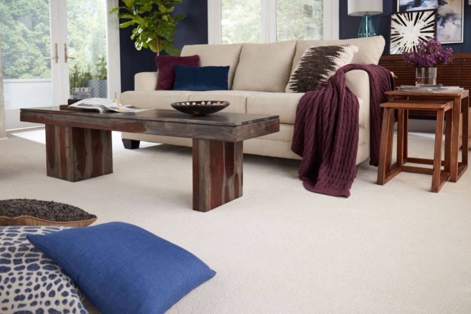 Living room scene with beige couch and white carpet with pillows on the ground